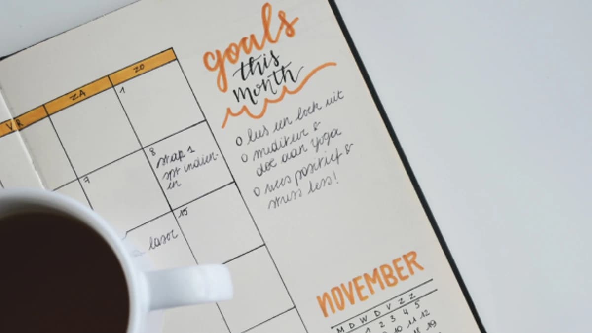 Planner open to a page with handwritten monthly goals beside a cup of coffee